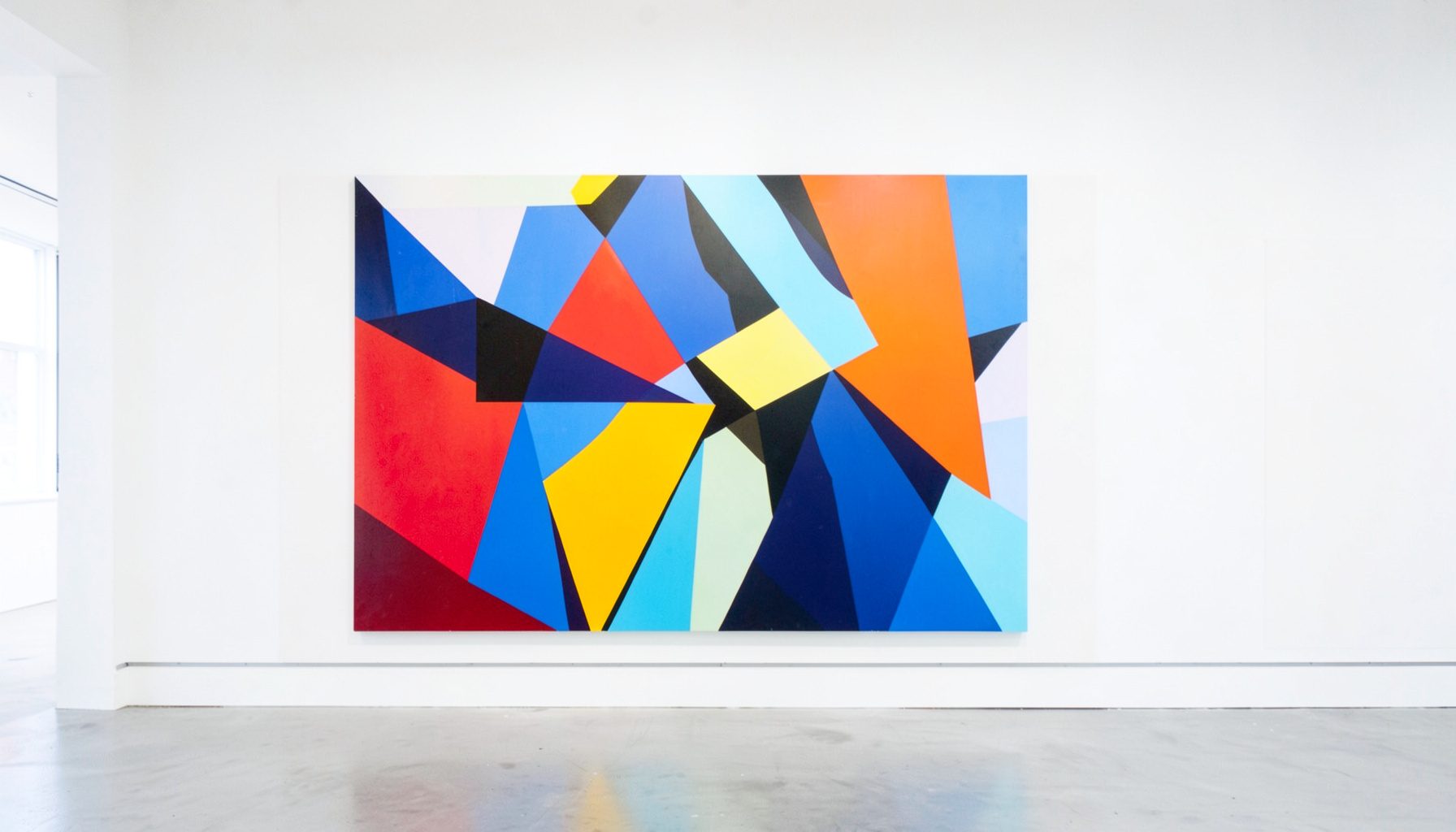 Abstract geometric painting with bold angular shapes in red, blue, yellow, and black against a white gallery wall, bright museum lighting