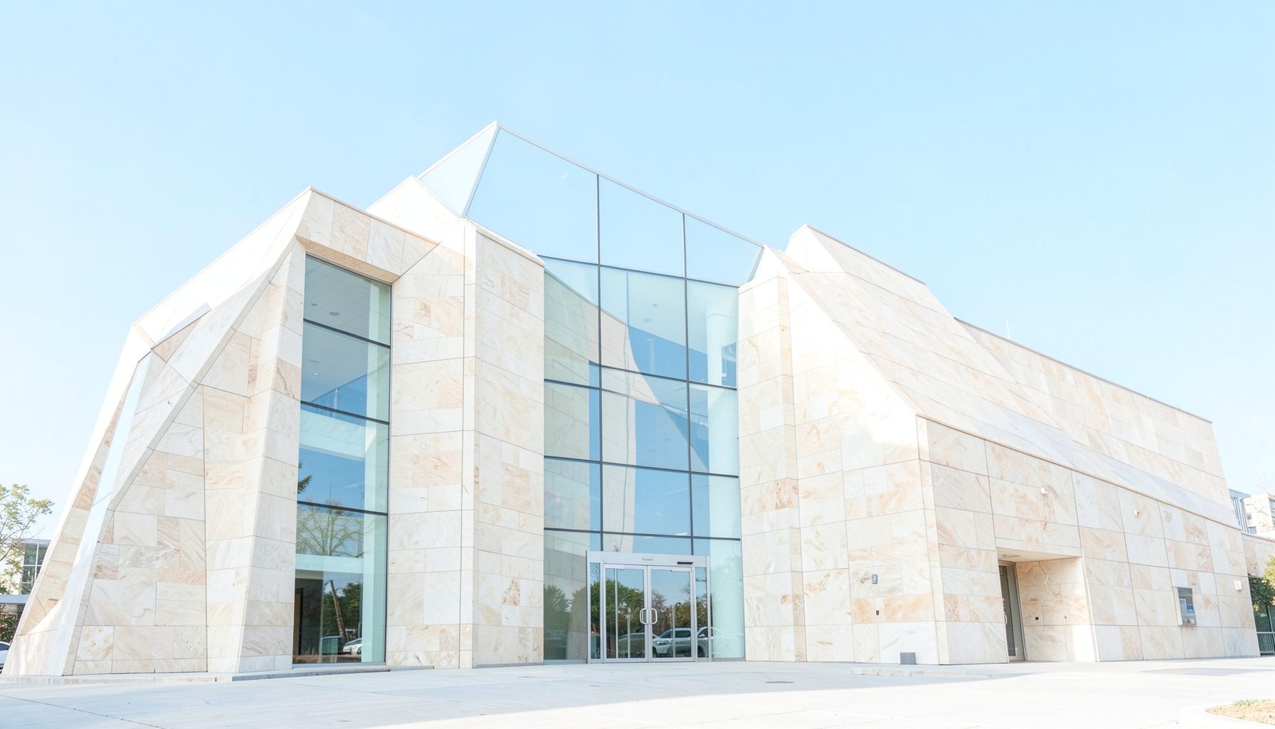 Sunlit exterior of a modern museum building with angular stone facade and large glass panels, clear blue sky