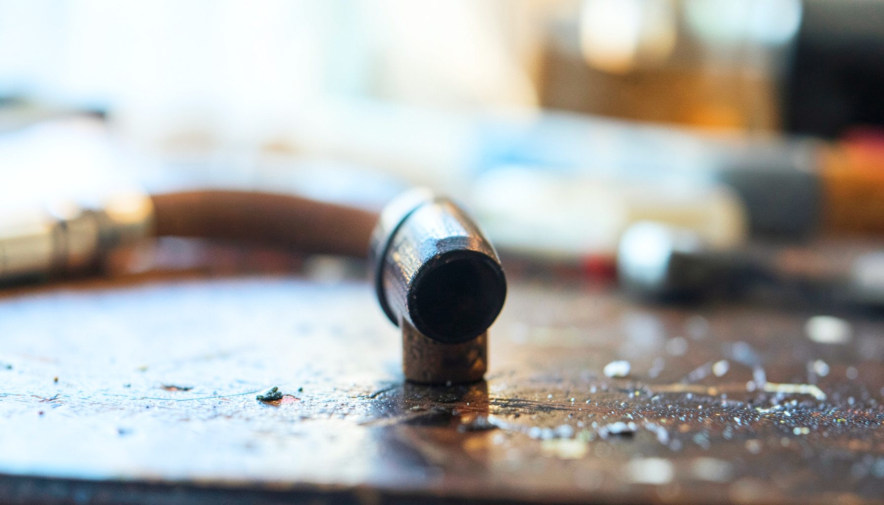 Close-up of a reed instrument mouthpiece on a dark workshop table, warm amber and brown tones, soft directional light