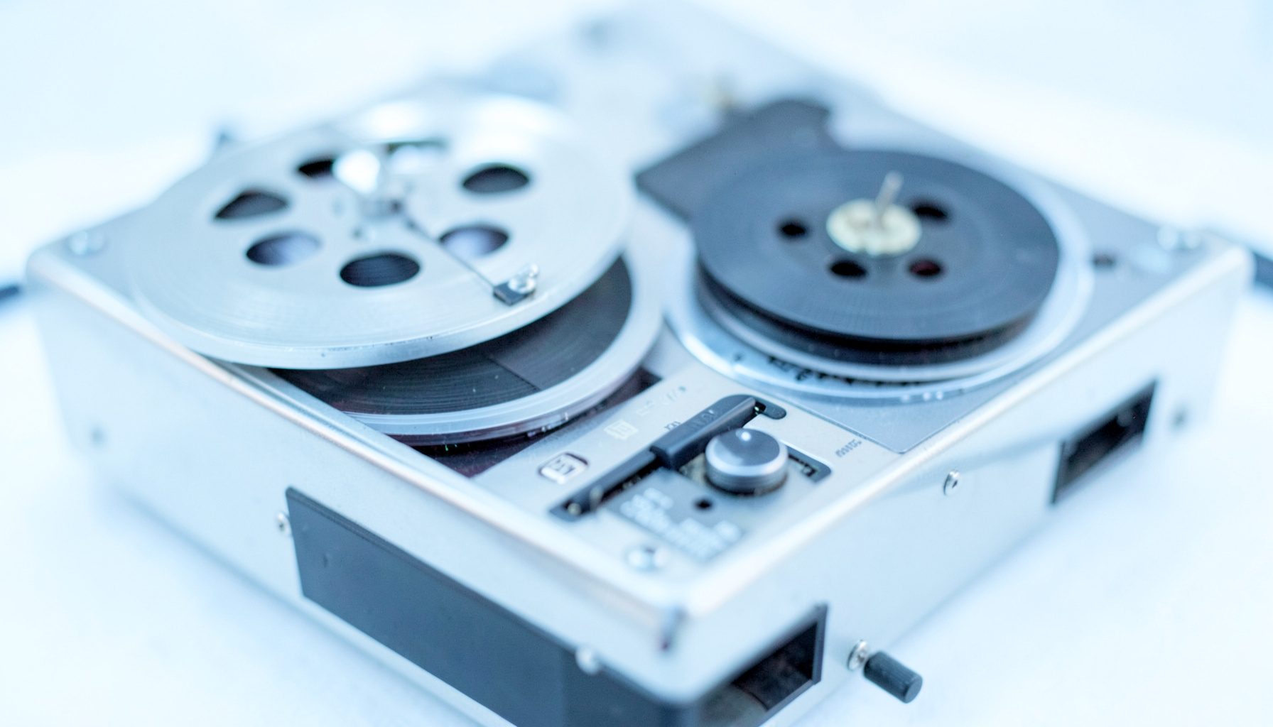 Close-up of a vintage reel-to-reel tape player with magnetic tape spooled, muted silver and charcoal tones